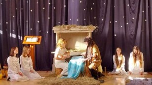 na scenie żłobek, postacie w kostiumach przedstawiające Józefa, Marię z lalką Jezusa, po bokach po dwie dziewczęta klęczą w białych sukienkach