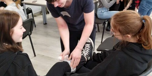 uczniowie siedzący w małych grupach bandażują sobie nawzajem ręce i nogi