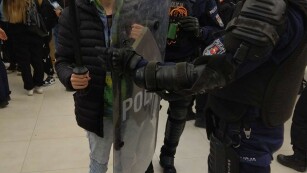 uczeń trzyma policyjną tarczę i pałkę, obok uzbrojeni policjanci