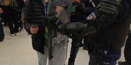 uczeń trzyma policyjną tarczę i pałkę, obok uzbrojeni policjanci