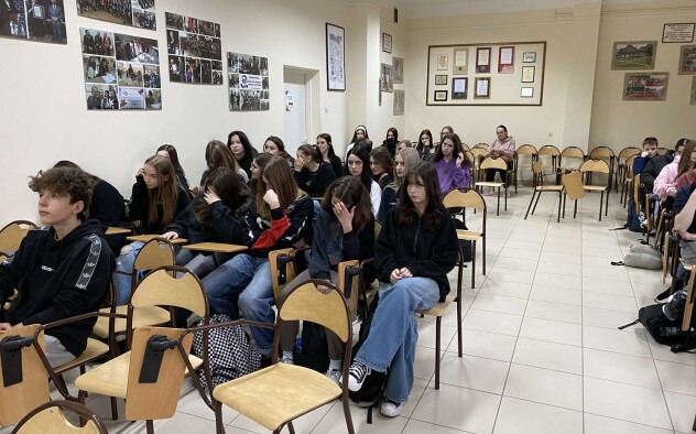 grupa uczniów w ławkach słucha wykładu- ujęcie rzędu pod ścianą