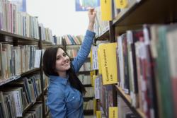 Uczennica w bibliotece sięgająca po ksiązki